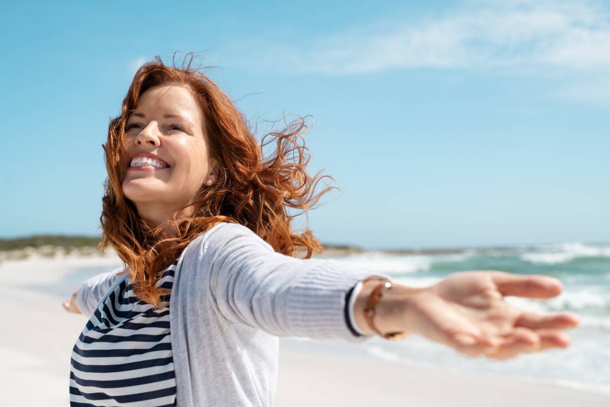 Woman excited and walking on the beach looking younger without surgery.